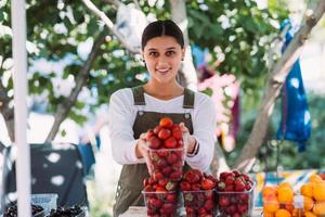 junge positive verkäuferin bei der arbeit, die erdbeeren in ihren händen hält foto