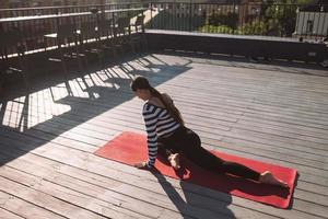 Frau, die am frühen Morgen Yoga-Übungen auf dem Hausdach macht foto