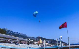 Mann sprang mit einem Fallschirm. Ein blauer Fallschirm fliegt zusammen mit einer Person durch den Himmel. aktive Erholung, Reisen in ein heißes Land, vor dem Hintergrund einer roten Fahne foto