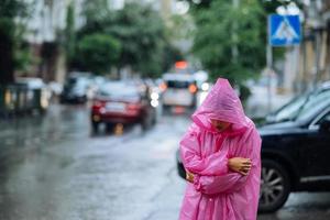 traurige Frau in einem Regenmantel auf der Straße im Regen foto