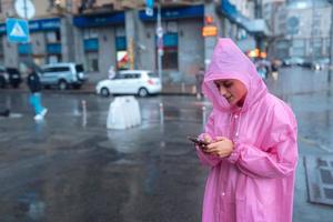 Eine junge Frau in einem Regenmantel schaut auf das Smartphone foto