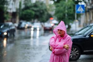 traurige Frau in einem Regenmantel auf der Straße im Regen foto