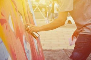 eine Hand mit einer Sprühdose, die ein neues Graffiti an die Wand malt. Foto des Prozesses des Zeichnens eines Graffitis auf einer Holzwand, Nahaufnahme. das konzept der straßenkunst und des illegalen vandalismus