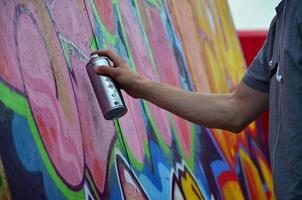 Ein junger rothaariger Graffiti-Künstler malt ein neues Graffiti an die Wand. Foto des Prozesses des Zeichnens eines Graffitis an einer Wand, Nahaufnahme. das konzept der straßenkunst und des illegalen vandalismus