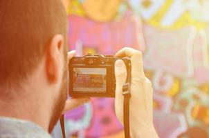 Ein junger Graffiti-Künstler fotografiert sein fertiges Bild an der Wand. Der Typ verwendet moderne Technologie, um eine farbenfrohe abstrakte Graffiti-Zeichnung aufzunehmen. Konzentrieren Sie sich auf das Aufnahmegerät foto