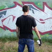 Ein junger Hooligan mit einer Spraydose steht an einer Betonwand mit Graffiti-Gemälden. illegales vandalismuskonzept. Straßenkunst foto