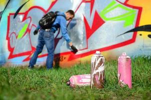 ein paar gebrauchte Farbdosen vor dem Hintergrund des Raums mit der Wand, auf der der junge Mann eine große Graffiti-Zeichnung zeichnet. moderne Kunst, Wände in Graffiti zu zeichnen foto