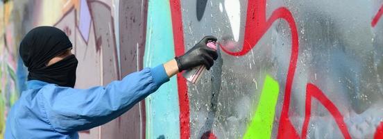 Ein junger Rowdy mit verstecktem Gesicht malt Graffiti auf eine Metallwand. illegales vandalismuskonzept foto