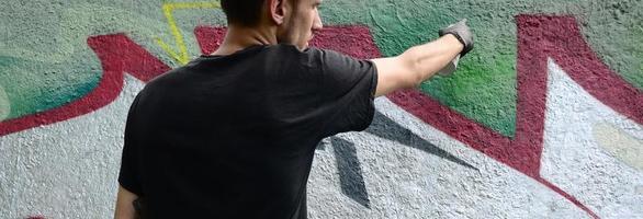 Ein junger Hooligan malt Graffiti auf eine Betonwand. illegales vandalismuskonzept. Straßenkunst foto