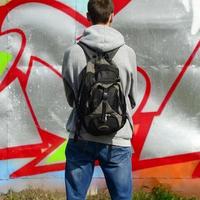 Ein junger Graffiti-Künstler mit einer schwarzen Tasche betrachtet die Wand mit seinem Graffiti an einer Wand. Street-Art-Konzept foto