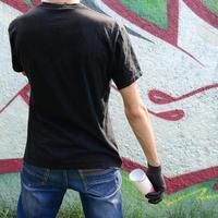 Ein junger Hooligan mit einer Spraydose steht an einer Betonwand mit Graffiti-Gemälden. illegales vandalismuskonzept. Straßenkunst foto