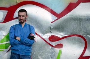 Der Graffiti-Künstler mit Spraydose posiert vor dem Hintergrund einer bunt bemalten Wand. Street-Art-Konzept foto