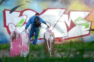 ein paar gebrauchte Farbdosen vor dem Hintergrund des Raums mit der Wand, auf der der junge Mann eine große Graffiti-Zeichnung zeichnet. moderne Kunst, Wände in Graffiti zu zeichnen foto