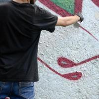 Ein junger Hooligan malt Graffiti auf eine Betonwand. illegales vandalismuskonzept. Straßenkunst foto