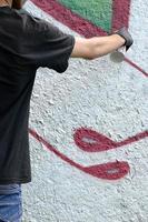 Ein junger Hooligan malt Graffiti auf eine Betonwand. illegales vandalismuskonzept. Straßenkunst foto