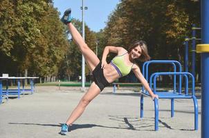 eine junge kaukasische Sportlerin in hellgrüner Sportkleidung, die Beinfahrten in der Sporthalle für aktive Erholung im Freien übt. sommersport und gesunder lebensstil foto