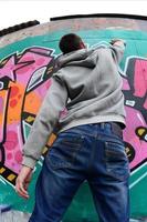 ein junger Mann in einem grauen Hoodie malt Graffiti in Pink und Grün c foto