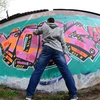 ein junger Mann in einem grauen Hoodie malt Graffiti in Pink und Grün c foto