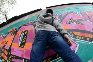 ein junger Mann in einem grauen Hoodie malt Graffiti in Pink und Grün c foto