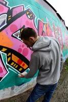 ein junger Mann in einem grauen Hoodie malt Graffiti in Pink und Grün c foto