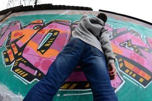 ein junger Mann in einem grauen Hoodie malt Graffiti in Pink und Grün c foto