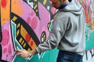 ein junger Mann in einem grauen Hoodie malt Graffiti in Pink und Grün c foto