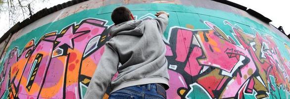 ein junger Mann in einem grauen Hoodie malt Graffiti in Pink und Grün c foto