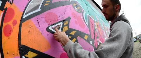 ein junger Mann in einem grauen Hoodie malt Graffiti in Pink und Grün c foto