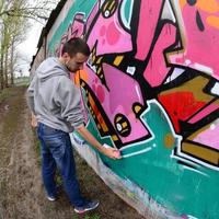 ein junger Mann in einem grauen Hoodie malt Graffiti in Pink und Grün c foto