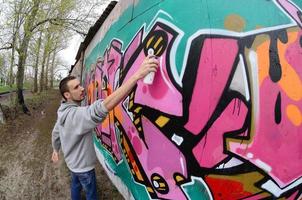 ein junger Mann in einem grauen Hoodie malt Graffiti in Pink und Grün c foto