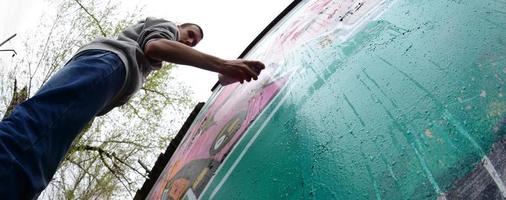 ein junger Mann in einem grauen Hoodie malt Graffiti in Pink und Grün c foto