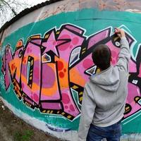 ein junger Mann in einem grauen Hoodie malt Graffiti in Pink und Grün c foto