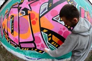 ein junger Mann in einem grauen Hoodie malt Graffiti in Pink und Grün c foto