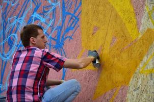 Ein junger rothaariger Graffiti-Künstler malt ein neues Graffiti an die Wand. Foto des Prozesses des Zeichnens eines Graffitis an einer Wand, Nahaufnahme. das konzept der straßenkunst und des illegalen vandalismus