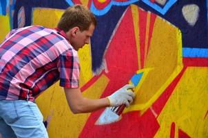 Ein junger rothaariger Graffiti-Künstler malt ein neues Graffiti an die Wand. Foto des Prozesses des Zeichnens eines Graffitis an einer Wand, Nahaufnahme. das konzept der straßenkunst und des illegalen vandalismus