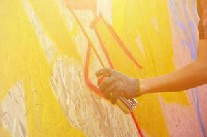 eine Hand mit einer Sprühdose, die ein neues Graffiti an die Wand malt. Foto des Prozesses des Zeichnens eines Graffitis auf einer Holzwand, Nahaufnahme. das konzept der straßenkunst und des illegalen vandalismus
