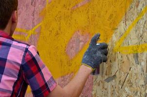 Ein junger rothaariger Graffiti-Künstler malt ein neues Graffiti an die Wand. Foto des Prozesses des Zeichnens eines Graffitis an einer Wand, Nahaufnahme. das konzept der straßenkunst und des illegalen vandalismus
