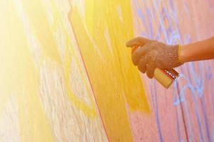 eine Hand mit einer Sprühdose, die ein neues Graffiti an die Wand malt. Foto des Prozesses des Zeichnens eines Graffitis auf einer Holzwand, Nahaufnahme. das konzept der straßenkunst und des illegalen vandalismus