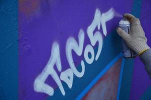 eine Hand mit einer Sprühdose, die ein neues Graffiti an die Wand malt. Foto des Prozesses des Zeichnens eines Graffitis auf einer Betonwand, Nahaufnahme. das konzept der straßenkunst und des illegalen vandalismus