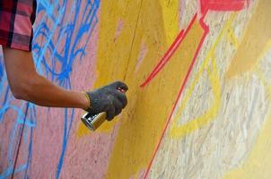 eine Hand mit einer Sprühdose, die ein neues Graffiti an die Wand malt. Foto des Prozesses des Zeichnens eines Graffitis auf einer Holzwand, Nahaufnahme. das konzept der straßenkunst und des illegalen vandalismus