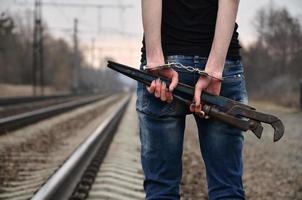 das Mädchen in Handschellen mit der Rohrzange auf dem Gleishintergrund. das Konzept der Kriminalprävention unter Beteiligung von Bahn und Zügen. foto