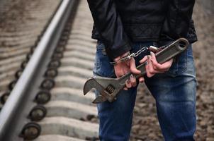 das Mädchen in Handschellen mit dem verstellbaren Schraubenschlüssel auf dem Gleishintergrund. das Konzept der Kriminalprävention unter Beteiligung von Bahn und Zügen. foto