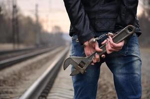 das Mädchen in Handschellen mit dem verstellbaren Schraubenschlüssel auf dem Gleishintergrund. das Konzept der Kriminalprävention unter Beteiligung von Bahn und Zügen. foto