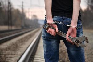 das Mädchen in Handschellen mit dem verstellbaren Schraubenschlüssel auf dem Gleishintergrund. das Konzept der Kriminalprävention unter Beteiligung von Bahn und Zügen. foto