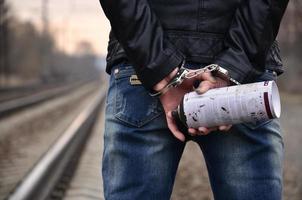 Mädchen in Handschellen mit Sprühdose auf dem Hintergrund einer Bahnstrecke. das Konzept der Vandalismusprävention unter Beteiligung von Bahn und Zügen. foto