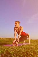 zwei junge blonde mädchen in sportanzügen praktizieren abends yoga auf einem malerischen grünen hügel unter freiem himmel. das konzept des sporttrainings im freien foto