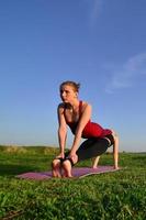 zwei junge blonde mädchen in sportanzügen praktizieren abends yoga auf einem malerischen grünen hügel unter freiem himmel. das konzept des sporttrainings im freien foto