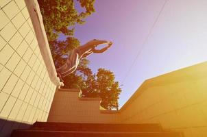 ein junger mann macht einen sprung durch den raum zwischen den betonbrüstungen. Der Athlet übt Parkour und trainiert unter Straßenbedingungen. Untersicht foto