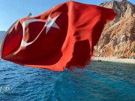 Türkische Flagge auf dem Hintergrund des Meeres und der Berge bei sonnigem Wetter foto