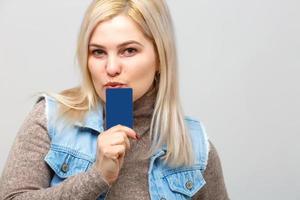 Porträt einer hübschen jungen Frau, die in einem Pullover gekleidet ist, der eine Kreditkarte auf ihrem Gesicht hält, isoliert auf weißem Hintergrund foto